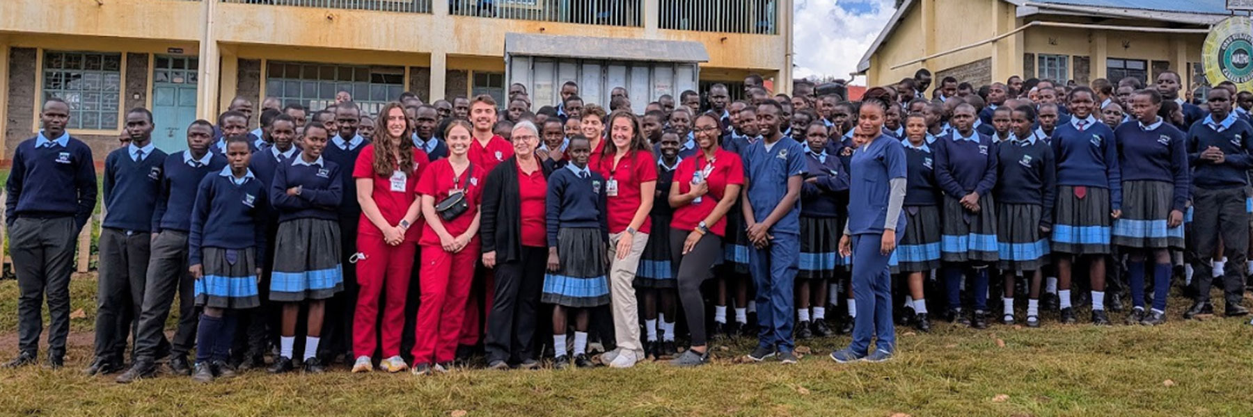 A group of IU School of Nursing students and faculty posing with uniformed high school students outside a school building in Kenya.