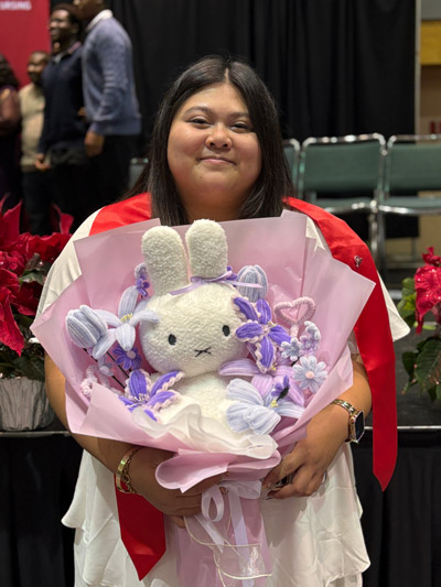 A December 2025 graduate poses for a photo while holding a flower bouquet during the IU School of Nursing in Indianapolis winter recognition ceremony.
